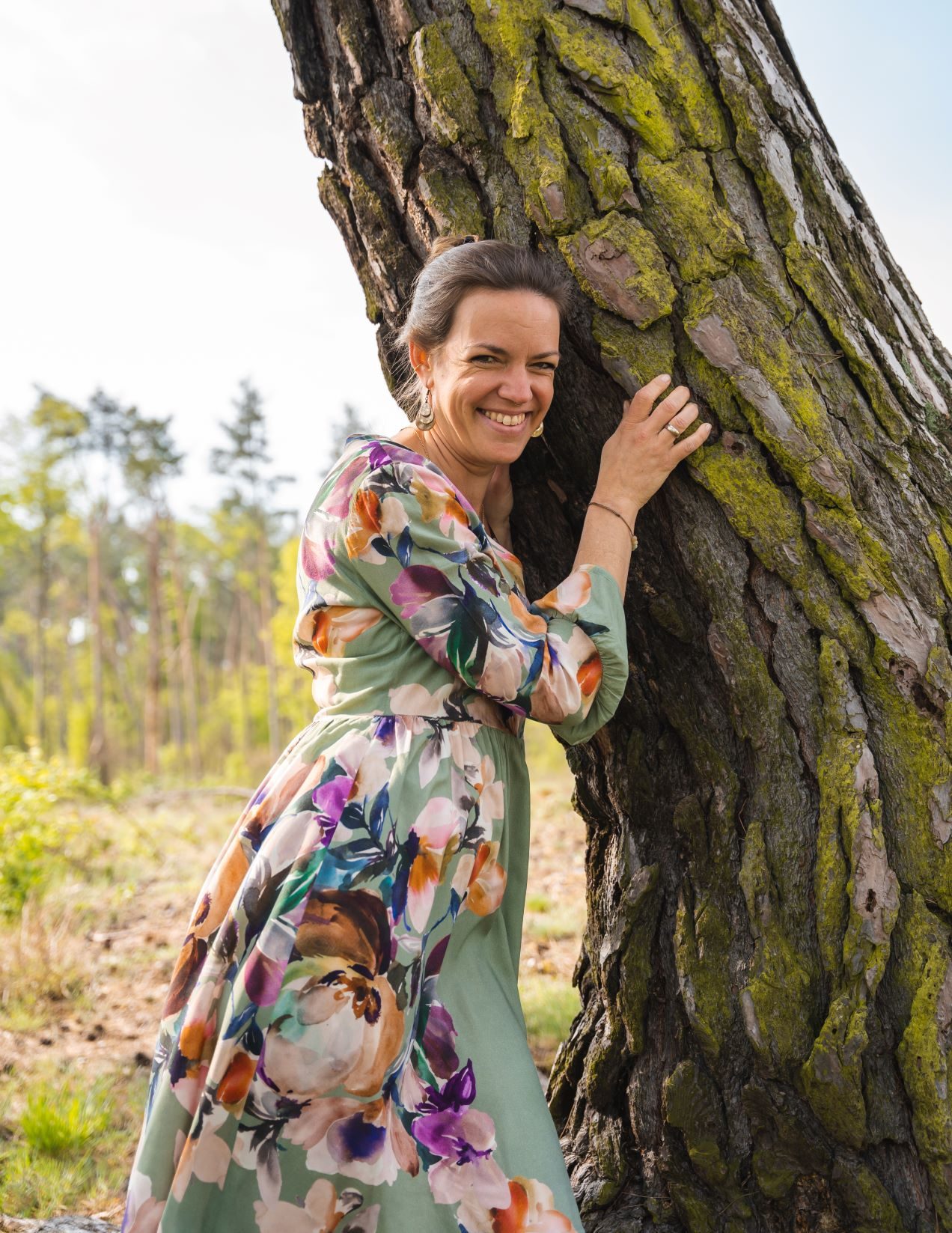 Steffi Mittenzwei lehnt lachend an einem alten, moosbewachsenen Baum