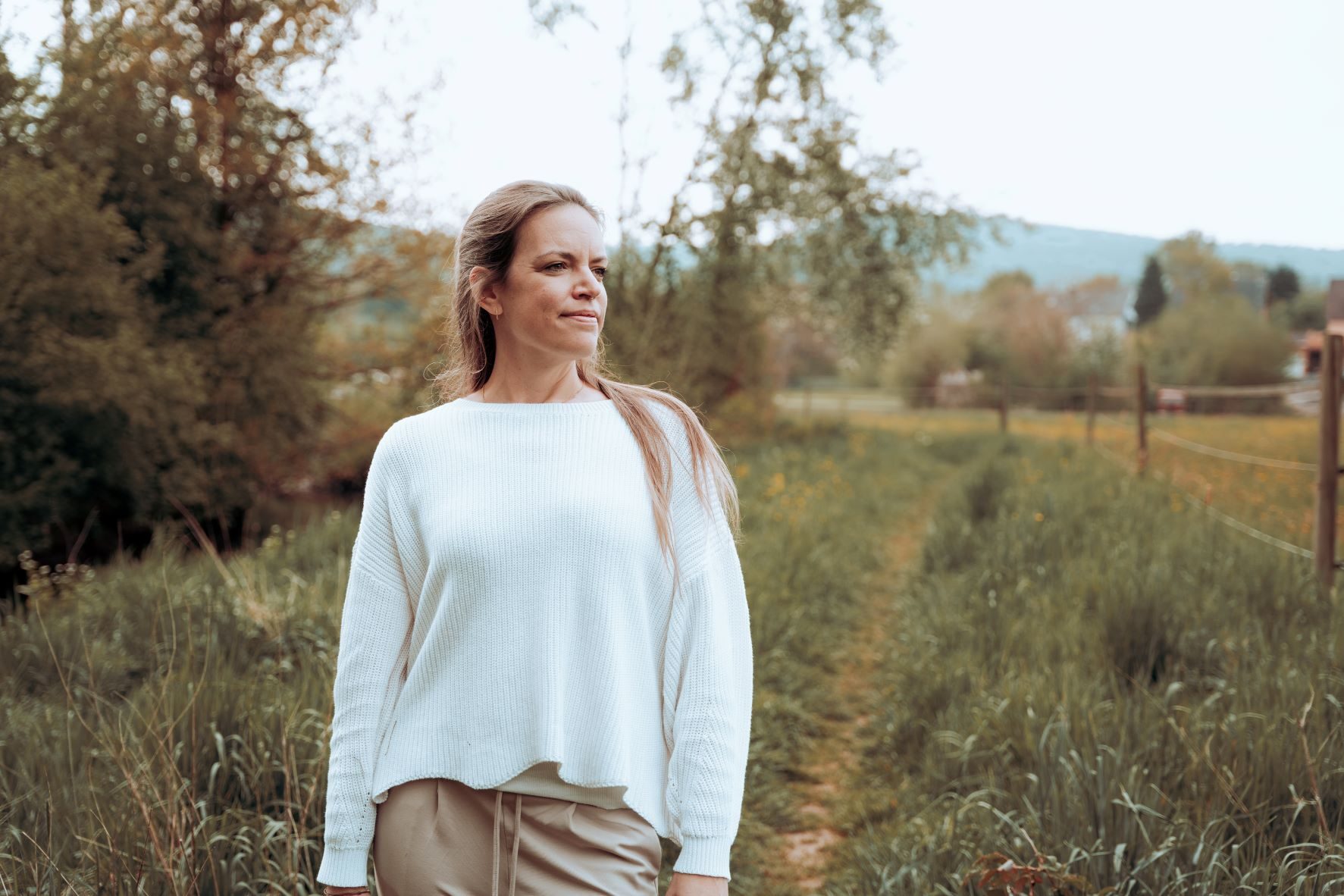 Steffi Mittenzwei steht nachdenklich auf einem Wiesenweg