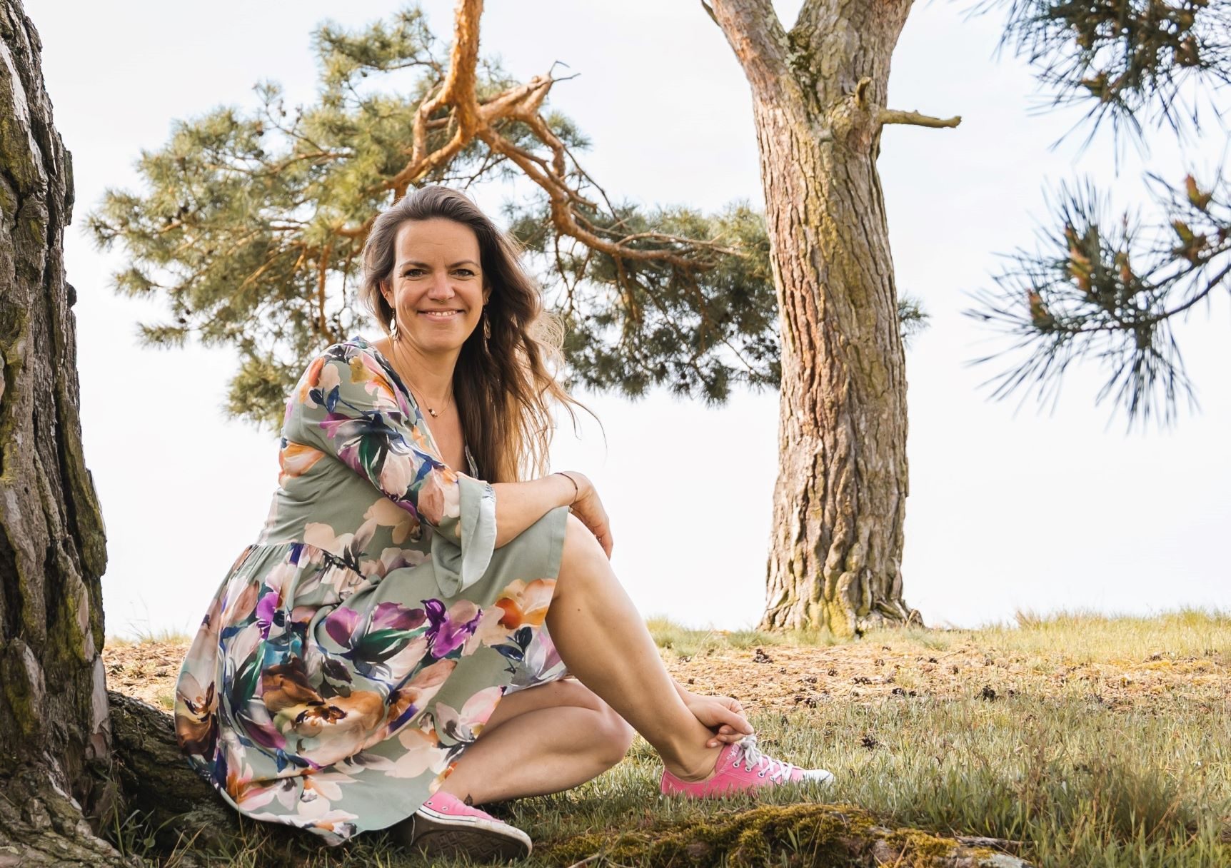 Steffi Mittenzwei sitzt lächelnd im bunten Kleid unter einer Kiefer