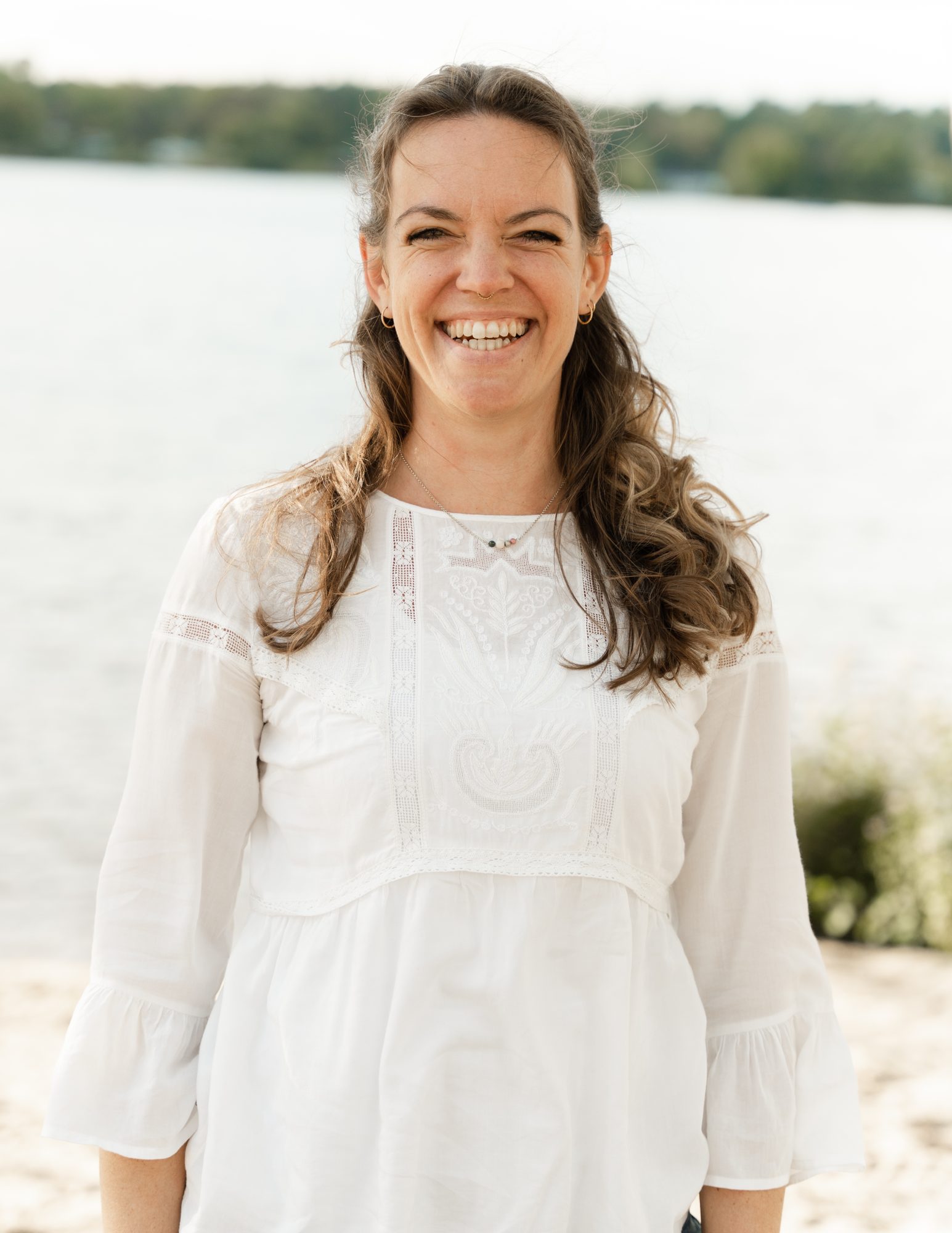Steffi Mittenzwei lacht in weißer Bluse an einem See